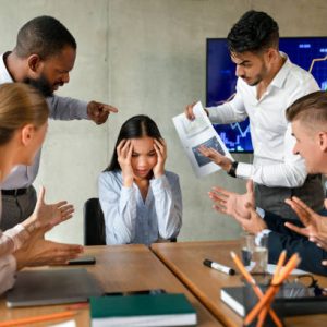 Conflicts At Work. Unhappy Asian Female Employee Suffering From Mobbing And Bullying In Office, Upset Employee Lady Covering Ears While Aggressive Coworkers Shouting At Her During Corporate Meeting